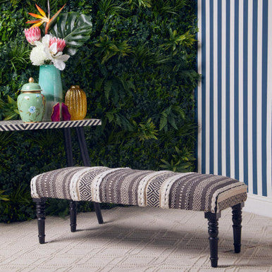 Decorative bench with striped pattern in a room with greenery and striped wall.