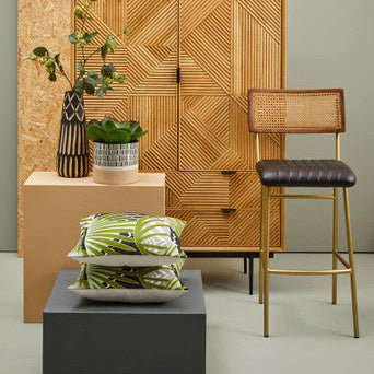 Wooden cabinet with decorative items, plants, and a bar stool in a room setting.