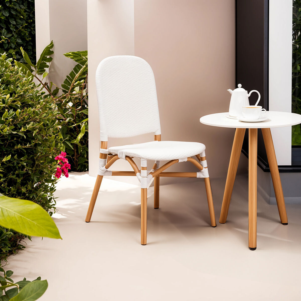 White chair and small round table with a teapot and cup on a light-colored floor with greenery.