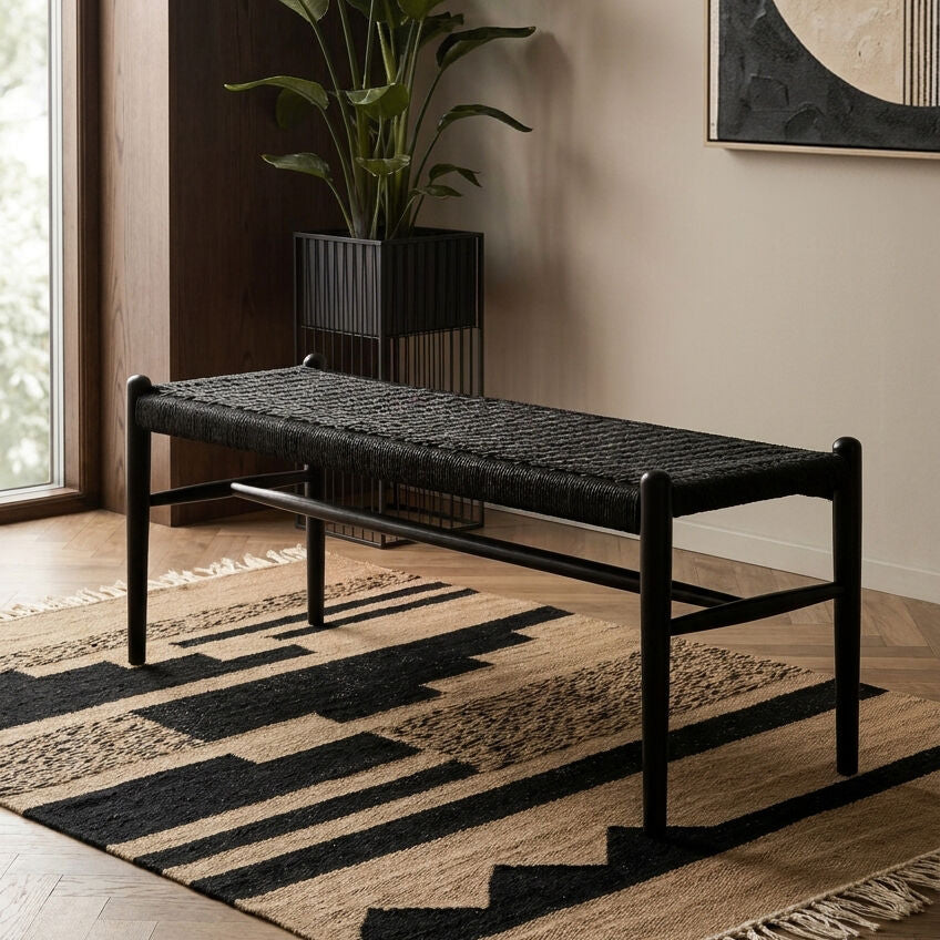 Black woven bench in a room with a plant and abstract art on the wall.