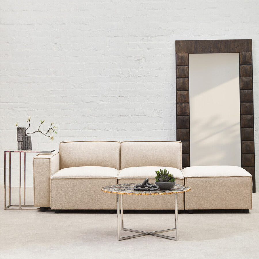 Beige sofa with a coffee table and decorative items against a light brick wall.