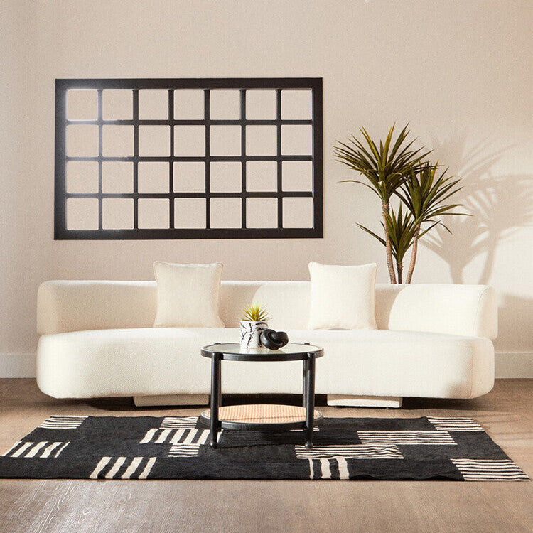 Modern living room with a white sofa, black coffee table, and decorative wall mirror.
