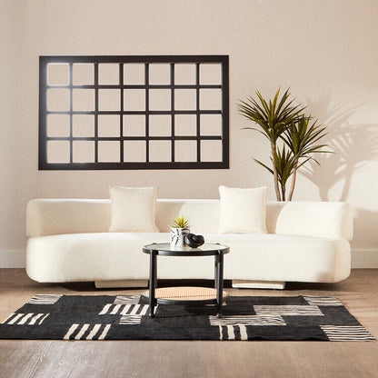Modern living room with a white sofa, black coffee table, and decorative wall mirror.
