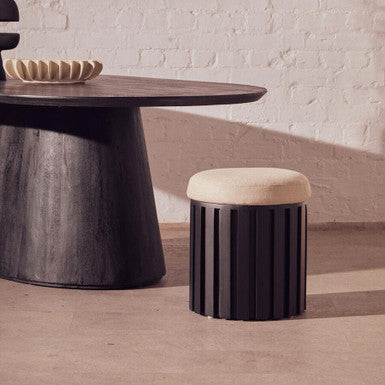 Modern black and beige stool in front of a round wooden table with abstract art on the wall.