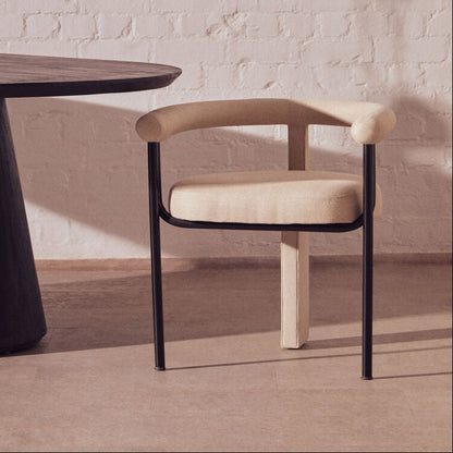 Modern chair with beige cushion and black frame next to a round wooden table in a room with abstract art on the wall.