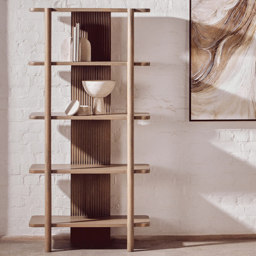 Wooden bookshelf against a white brick wall with abstract art on the wall.