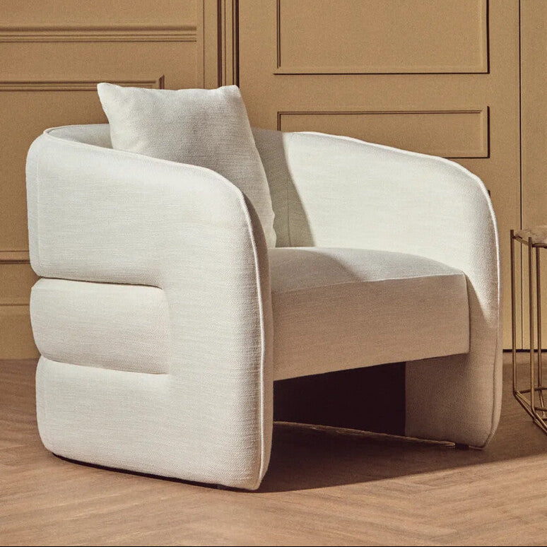 Modern beige armchair in a room with wooden paneling and a vase on a side table.