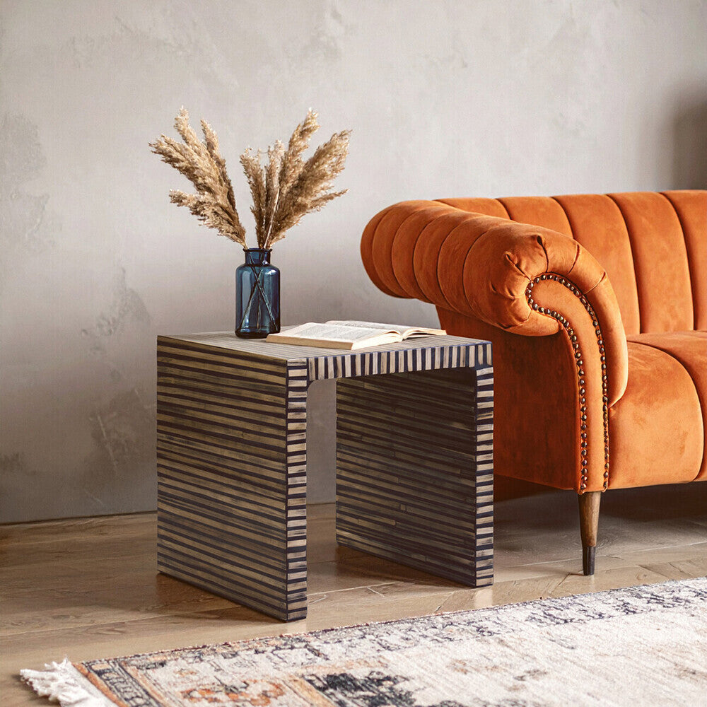 Wooden side table with decorative items next to an orange sofa in a room.