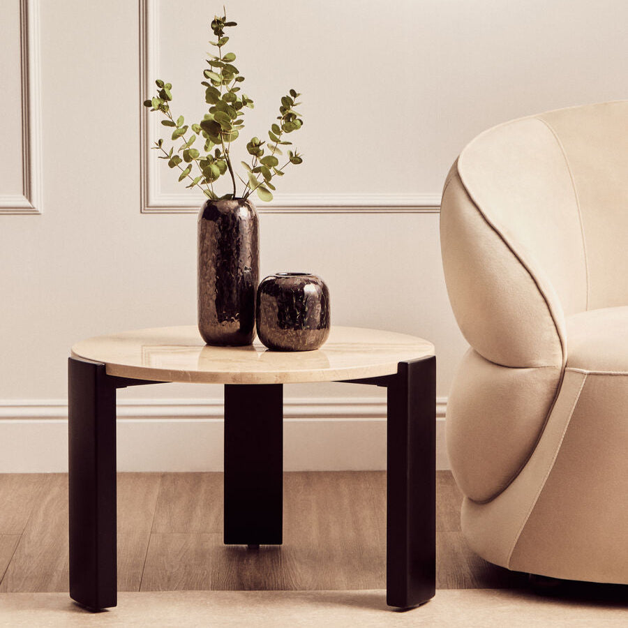 Round wooden side table with two vases and a plant in a living room setting.
