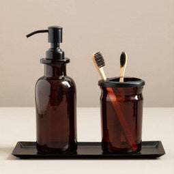 Brown glass bottle with pump, toothbrush holder with toothbrushes, and black tray on a beige background