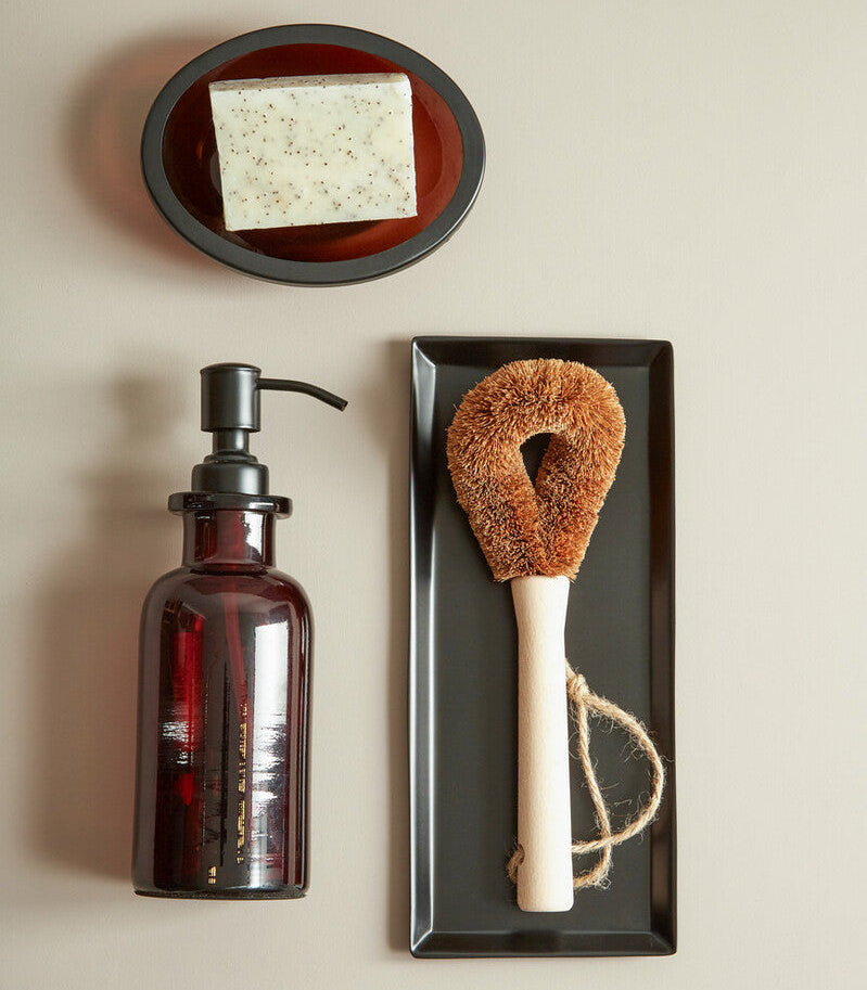 Bottle, soap dish with bar of soap, and natural brush on a beige background