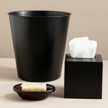 Black trash can, black cube with white tissues, and small black dish on a beige surface.