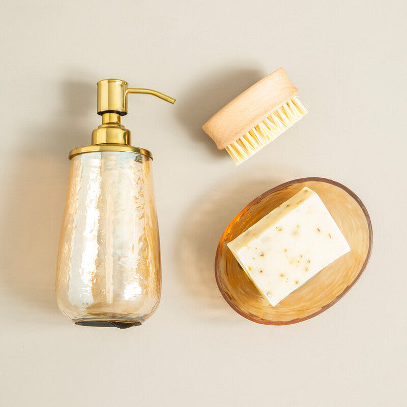 Gold soap dispenser, brush, and soap bar on a beige background