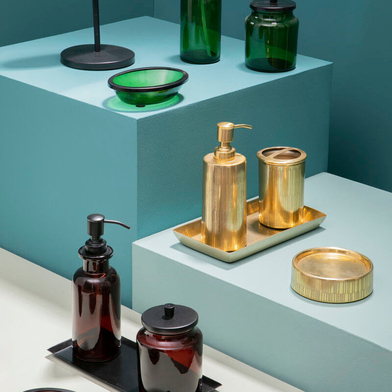 Bathroom accessories including bottles, a mirror, and a tray on a teal wall background.