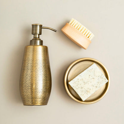 Brass soap dispenser with a brush and soap bar on a beige background