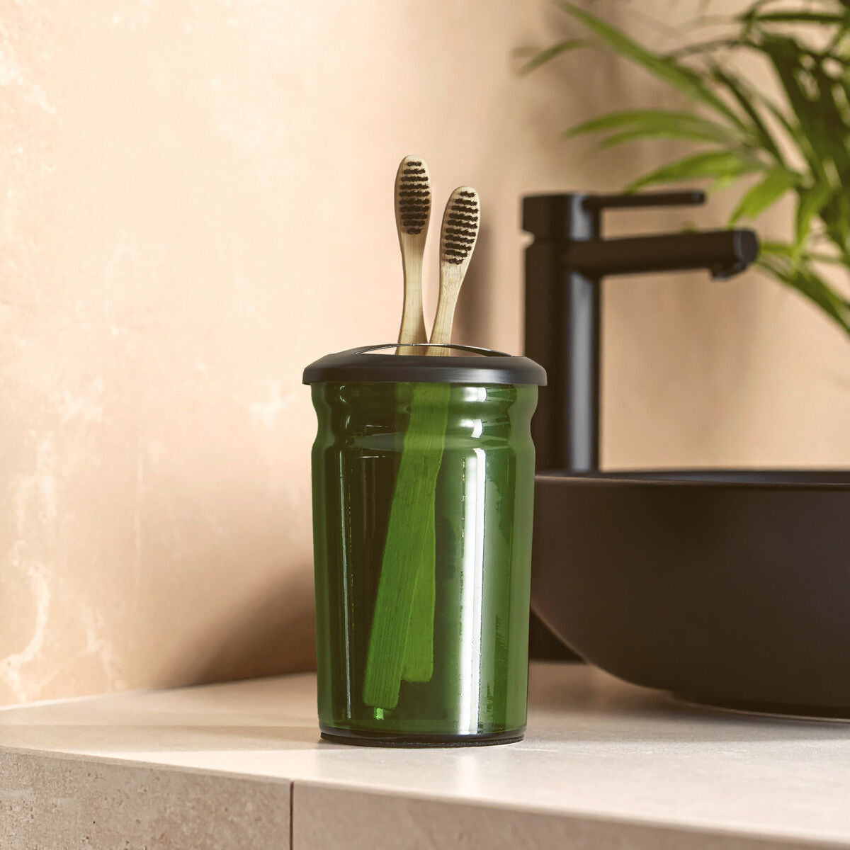 Green glass container with toothbrushes on a bathroom counter
