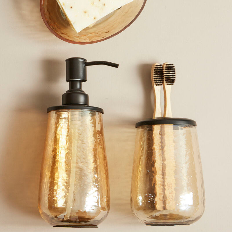 Bathroom accessories including a soap dispenser, toothbrush holder, and soap on a beige wall.
