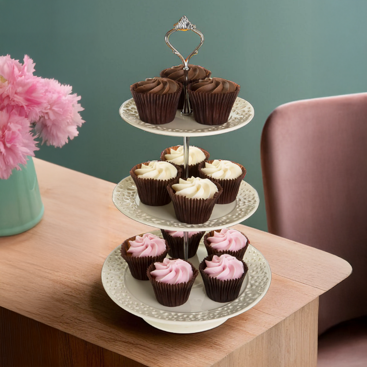 Three-tiered cake stand with cupcakes on a wooden table against a green wall.