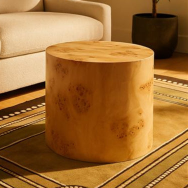 Wooden stool on a patterned rug with a beige sofa and plant in the background