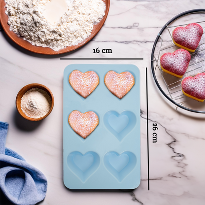 Heart-shaped silicone mold with measurements on a kitchen counter with baking ingredients and pastries.