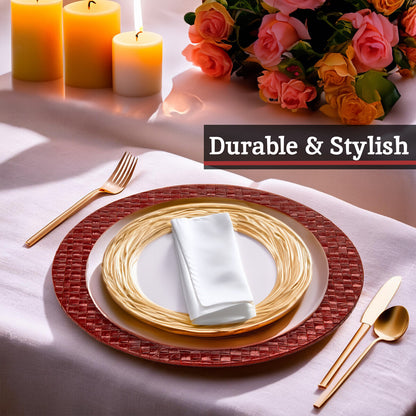 Table setting with red woven placemat, gold plates, white napkin, and cutlery on a white tablecloth with candles and flowers.