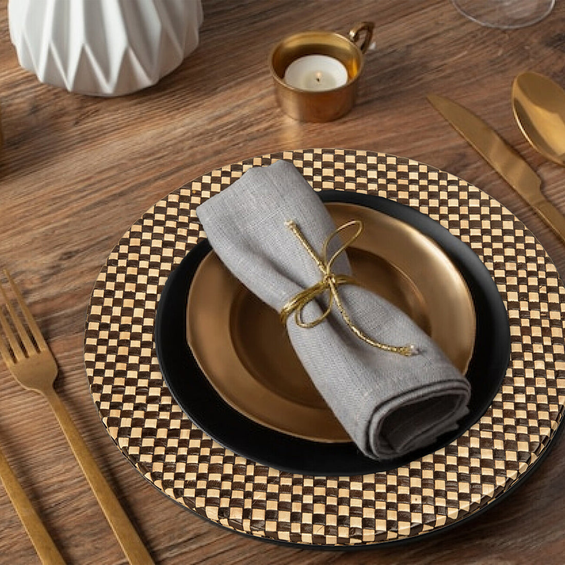 Dining table setting with gold and black plates, gray napkin, and checkered placemat.
