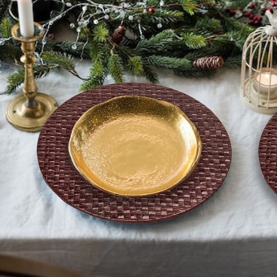 Decorative table setting with gold plate, candles, and greenery on a white tablecloth.