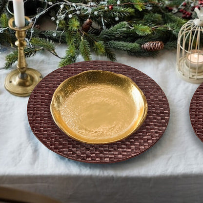 Decorative table setting with gold plate, candles, and greenery on a white tablecloth.