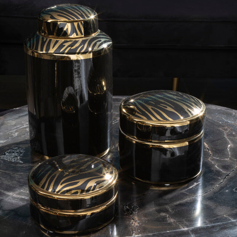Set of black and gold decorative jars on a dark surface with a blurred background