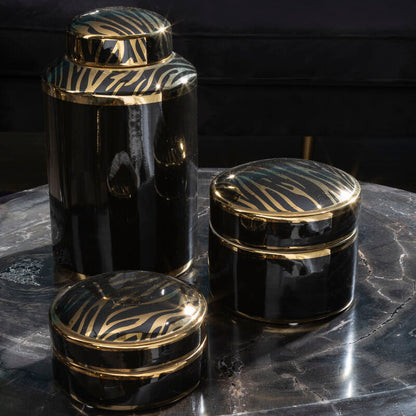 Set of black and gold decorative jars on a dark surface with a blurred background