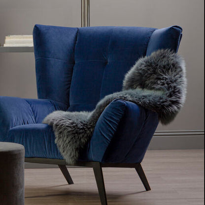Blue armchair with gray fur throw and gray ottoman in a room with a glass shelf.