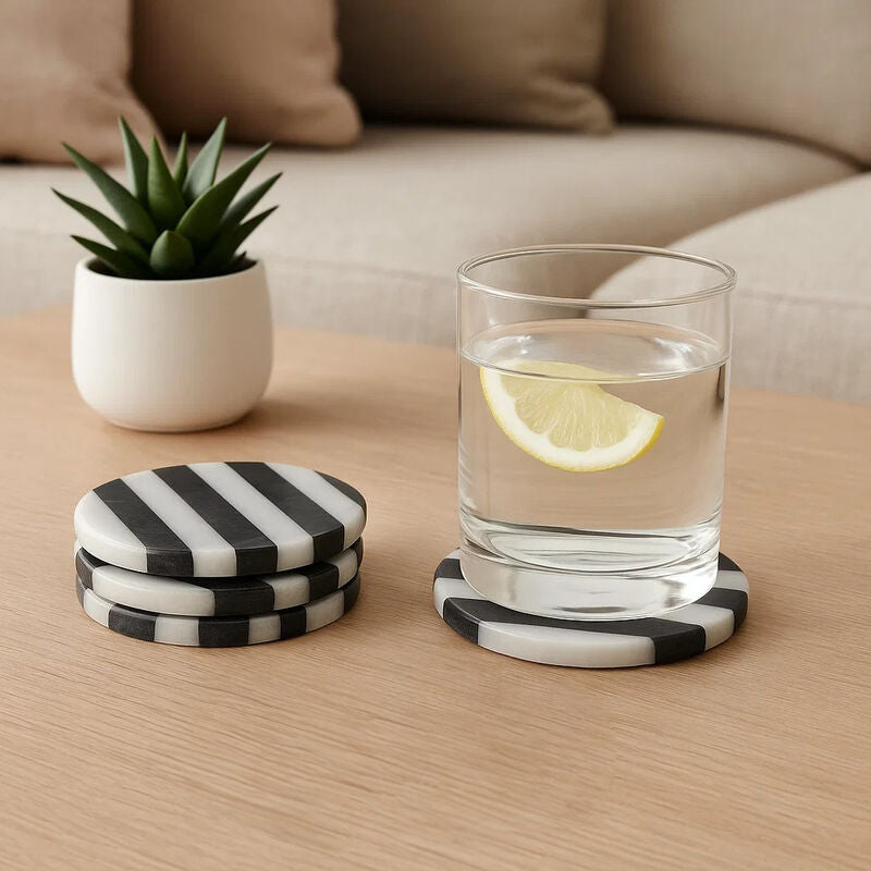 Set of black and white striped coasters with a glass of water and lemon on a wooden table.
