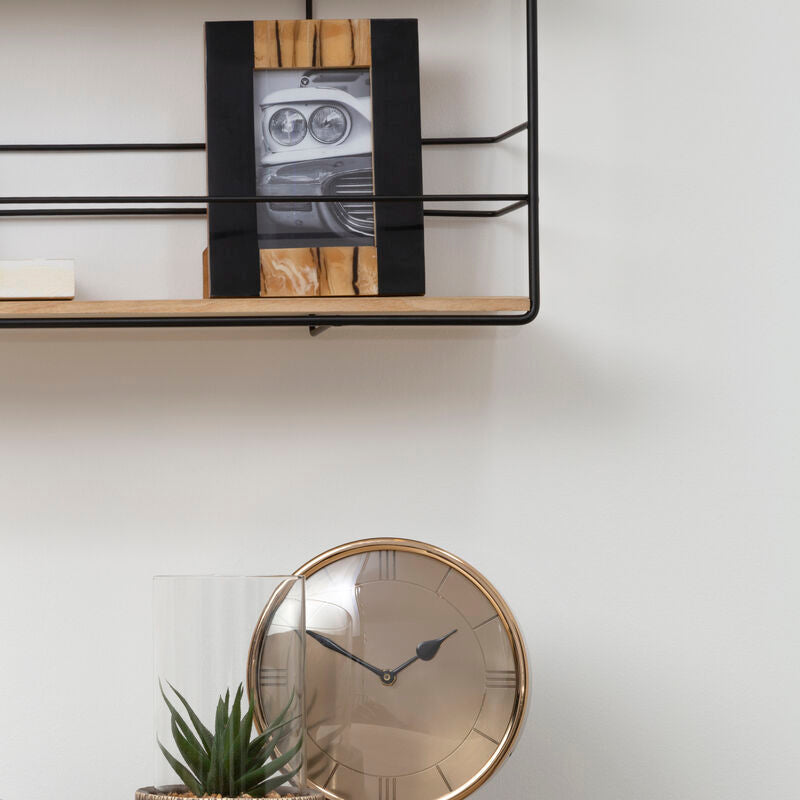 Wooden desk with clock, plant, and picture frame against a white wall