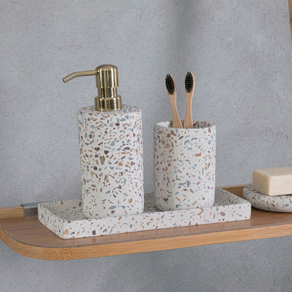 Bathroom accessories including a terrazzo-patterned soap dispenser, toothbrush holder, and soap on a wooden shelf against a gray wall.