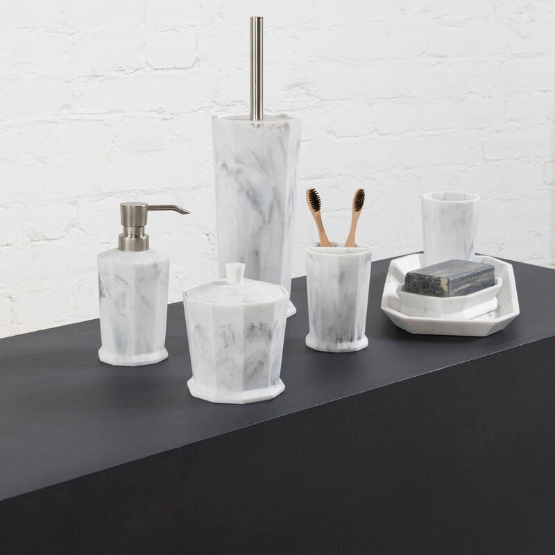 Bathroom accessories including a soap dispenser, toothbrush holder, and soap dish on a dark surface with a white brick wall background.